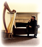 Noah Brenner sits and looks thoughtfully at his harp from the other end of a couch.